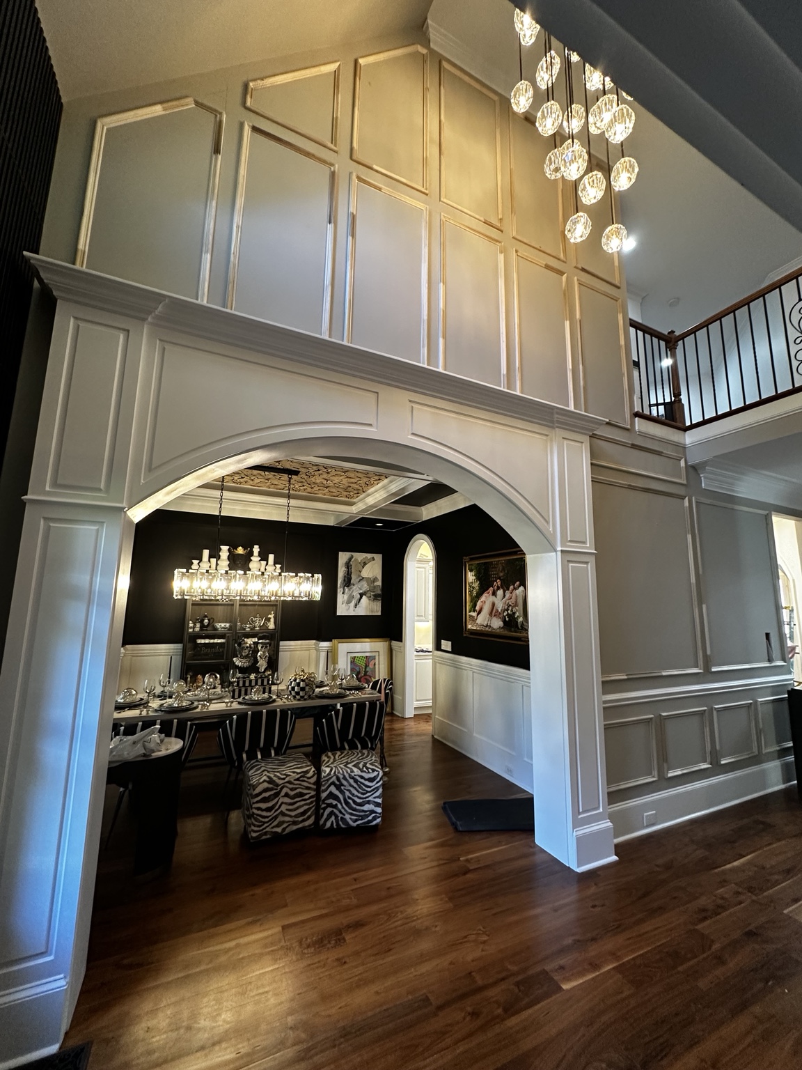 Wide white trimmed archway into the dining room with wall molding extending to the upper landing
