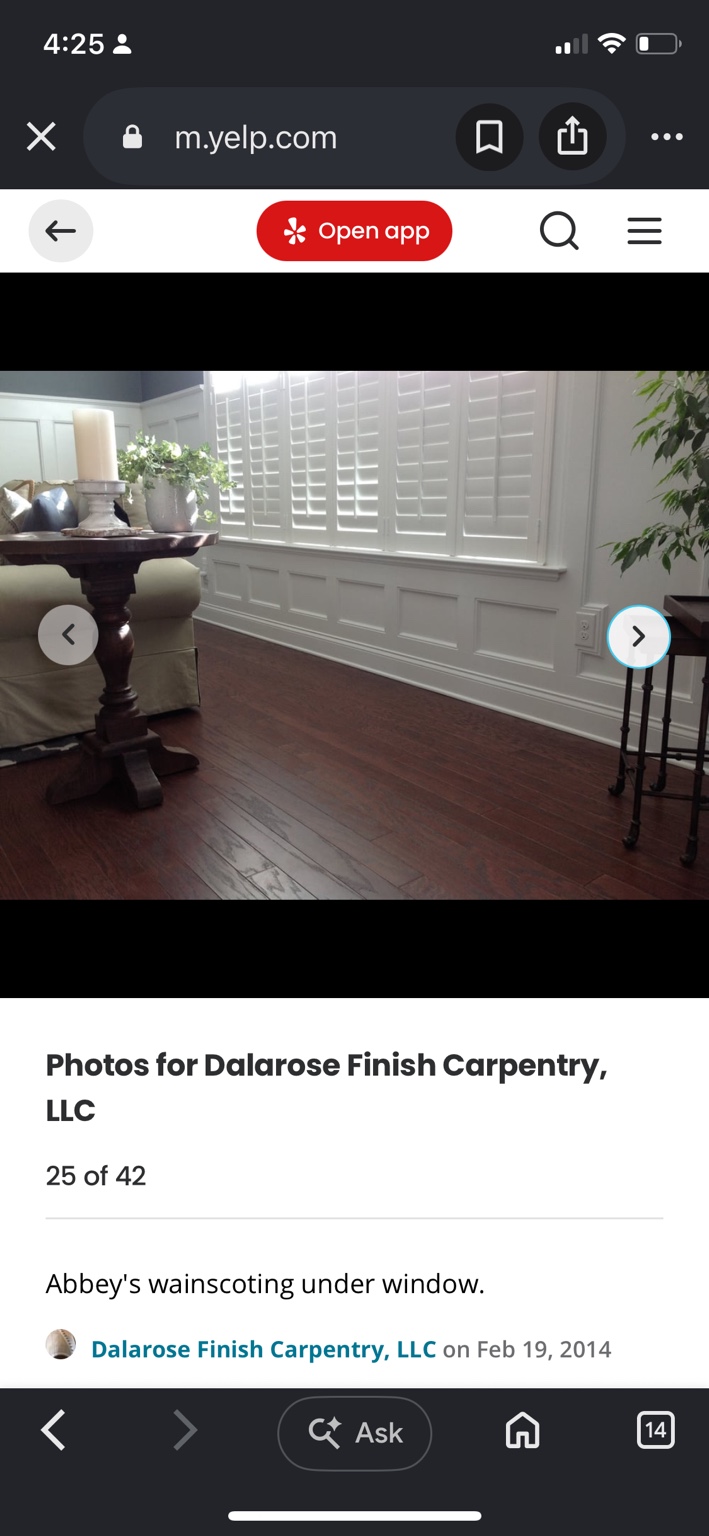White picture-frame wainscoting beneath a wide living-room window with plantation shutters