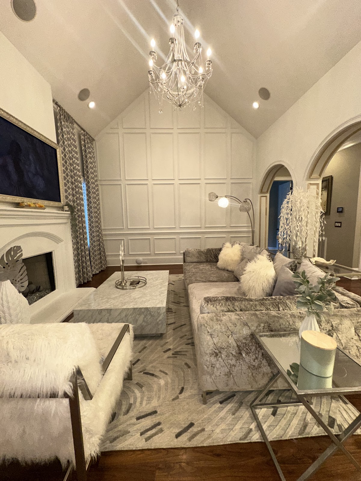 Living room with white picture-frame wall molding extending to a vaulted ceiling, a chandelier and arched doorways