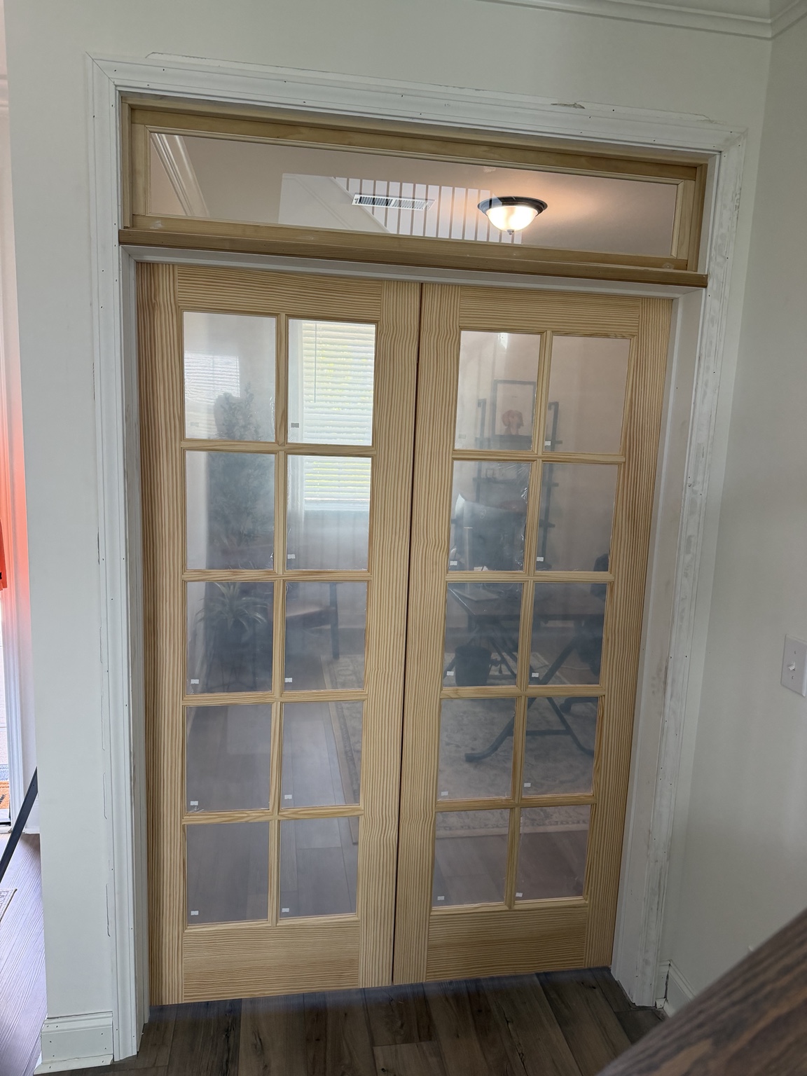 New unfinished wood and glass double doors with an upper transom window seen from the hall